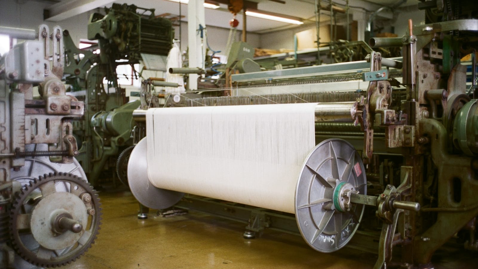 Weaving looms with a large roll of white fabric in a textile mill