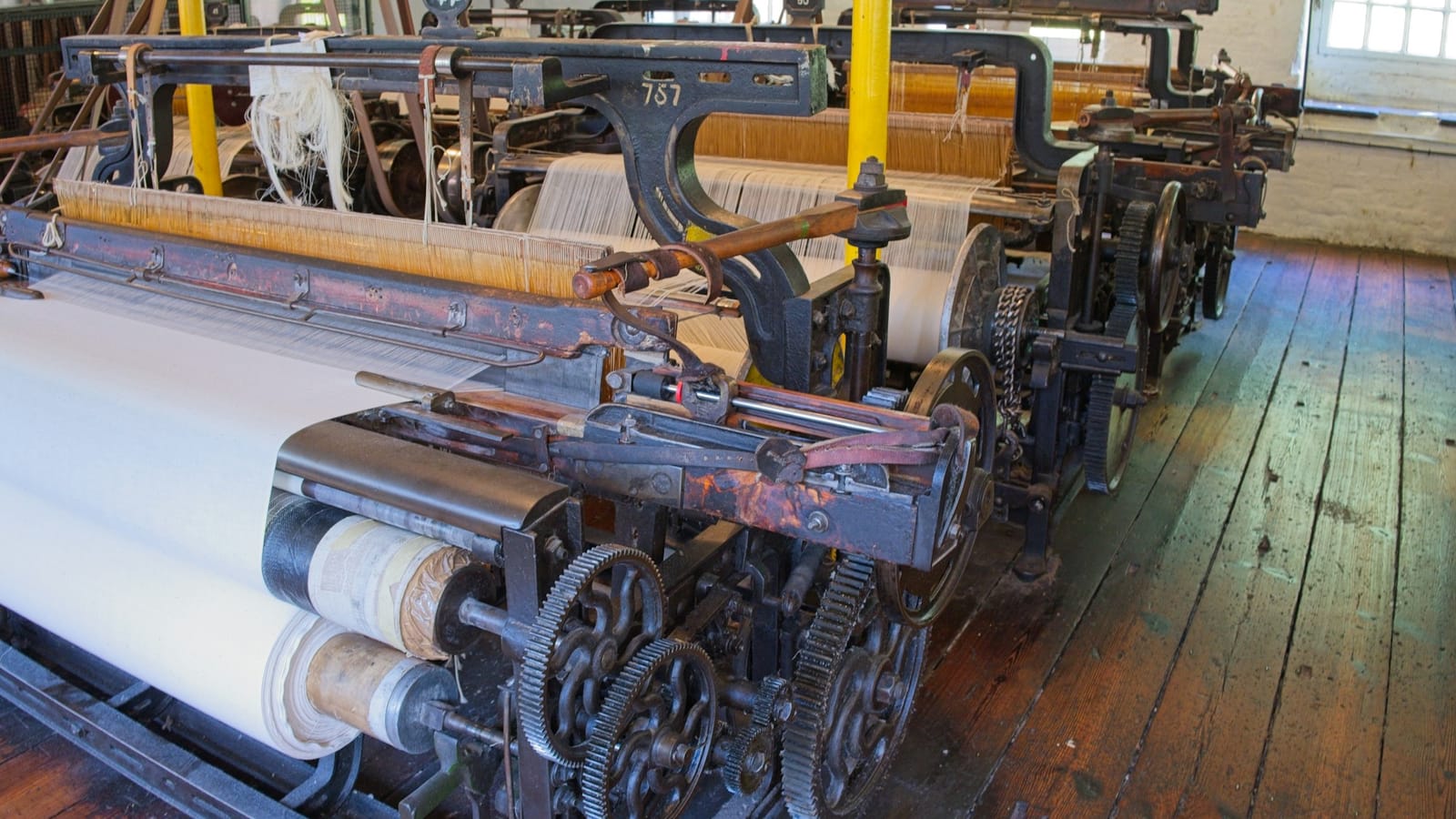 Older weaving machinery with fabric rolls in a textile mill