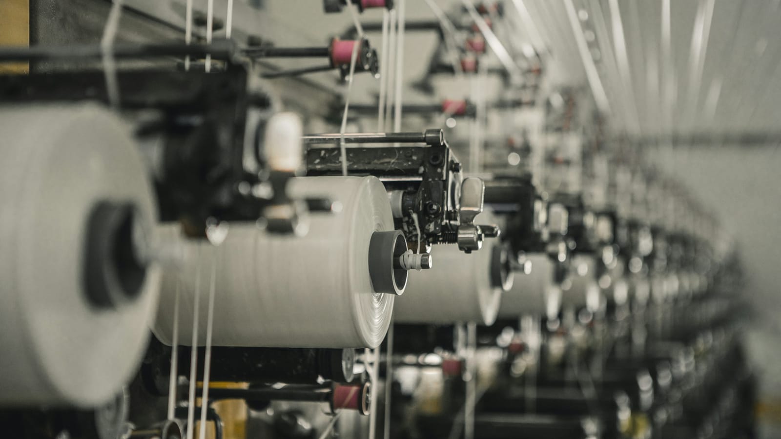 Rows of winding machines with white yarn packages in a modern spinning mill